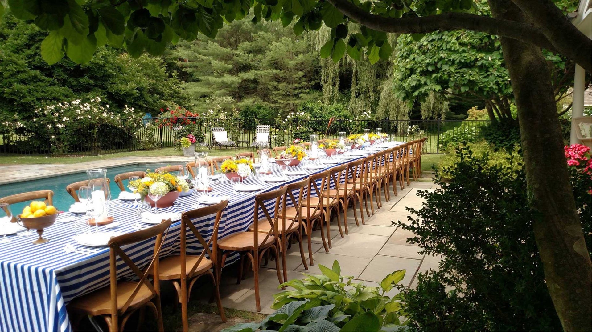 A party setup poolside featuring blue and white striped tables and center pieces full of lemons.
